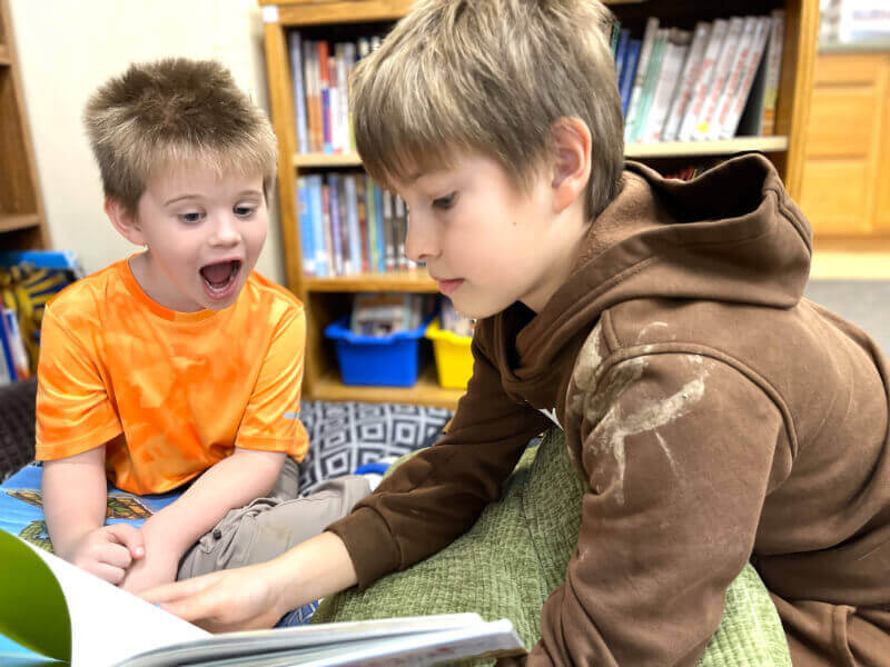 Two boys reading a book together in a classroom